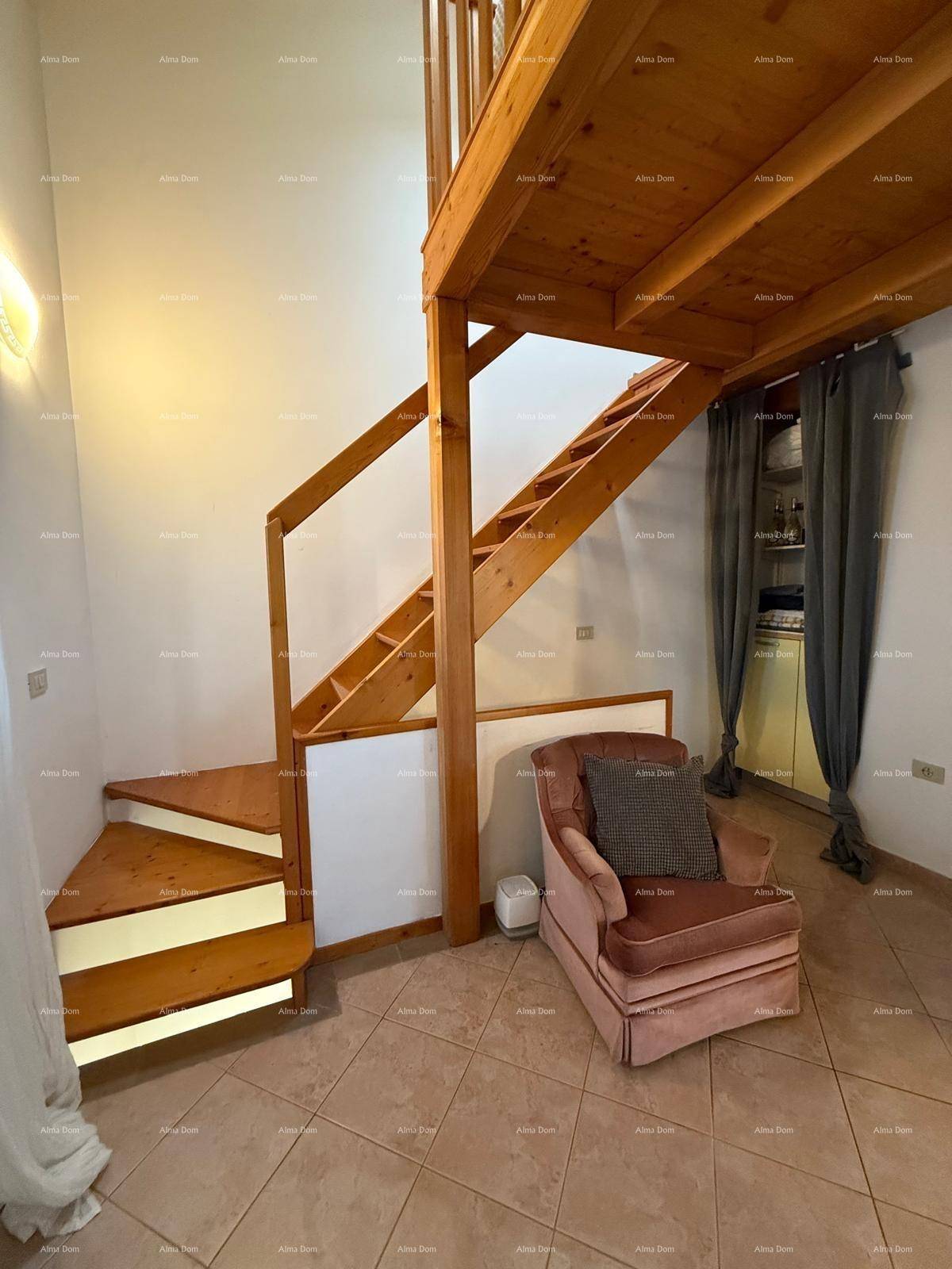 Wohnbereich mit Holztreppe zum Obergeschoss und einem bequemen Sessel, Fliesenboden.