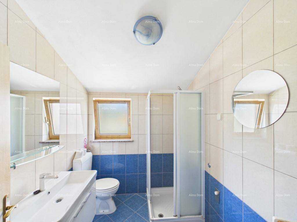Badezimmer mit blauen und beigen Fliesen, Dusche, WC und Fenster für Tageslicht.