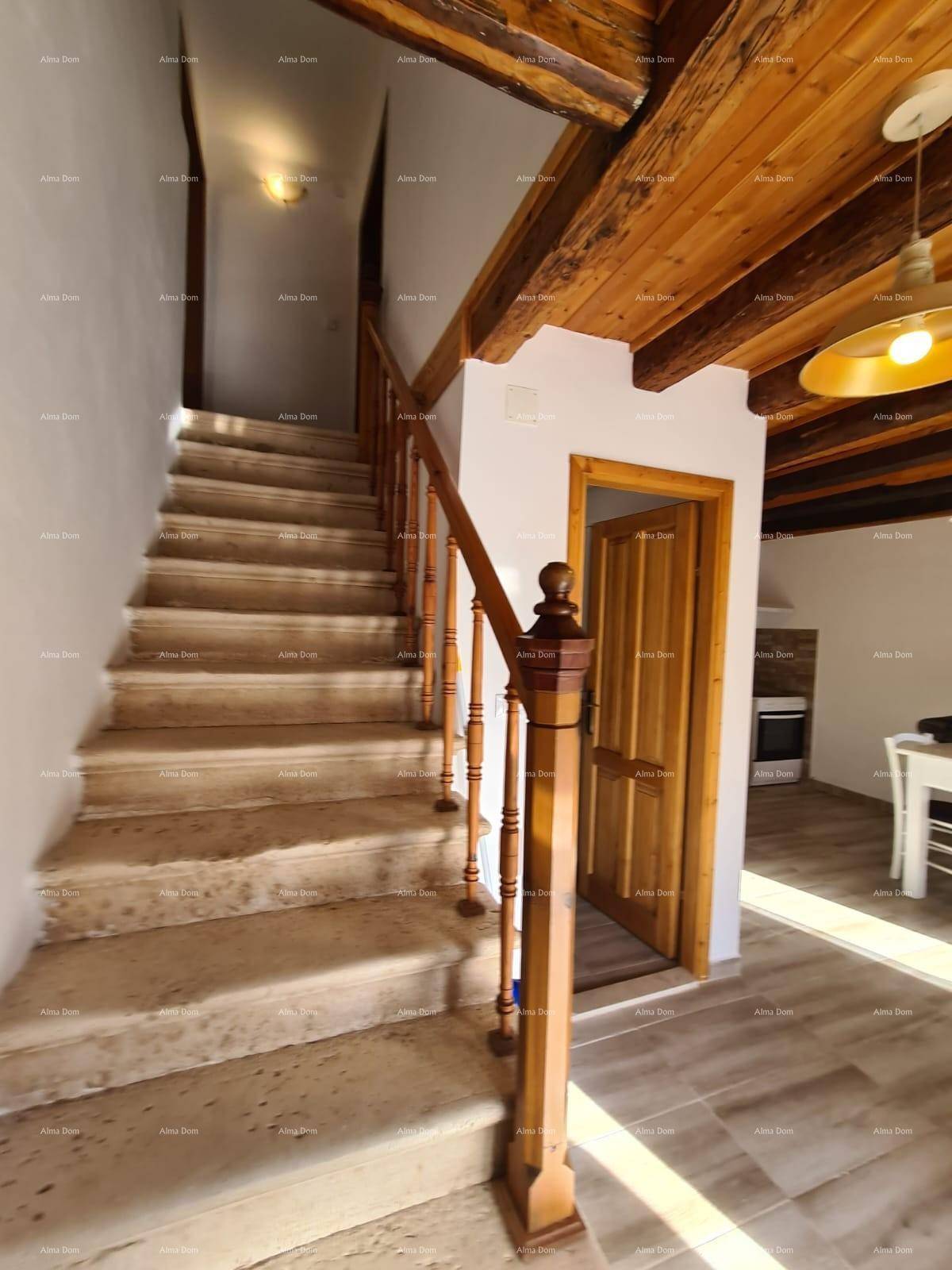 Rustikale Steintreppe mit Holzgeländer führt nach oben, ergänzt durch Holzbalkendecke und hellen Boden.