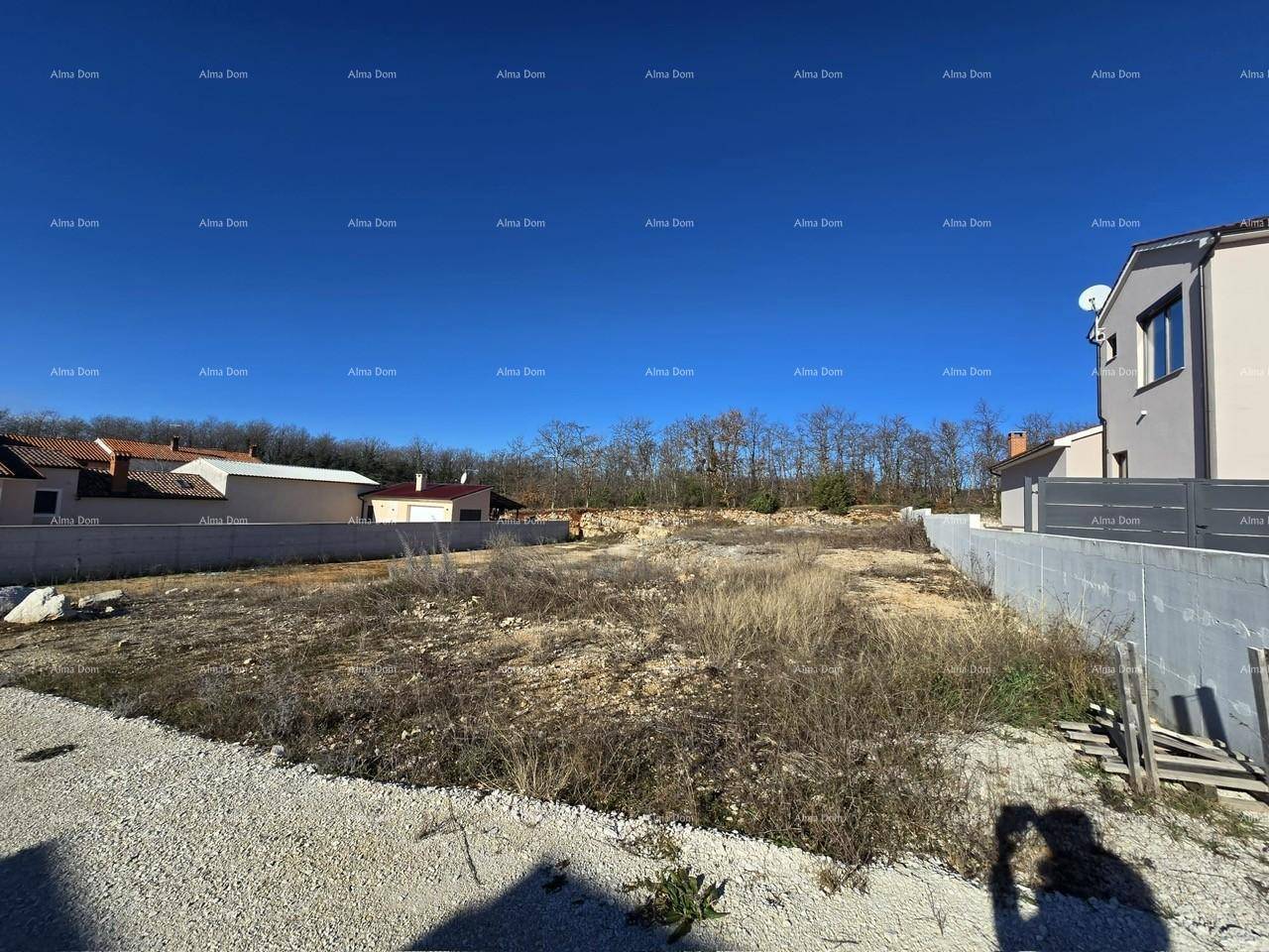 Blick über ein unbebautes Grundstück mit trockener Vegetation und angrenzenden Gebäuden.