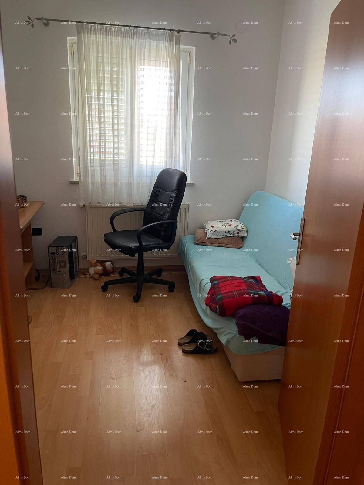 Zimmer mit Schlafsofa, Bürostuhl und Schreibtisch, ausgestattet mit hellem Holzfußboden und Fenster.
