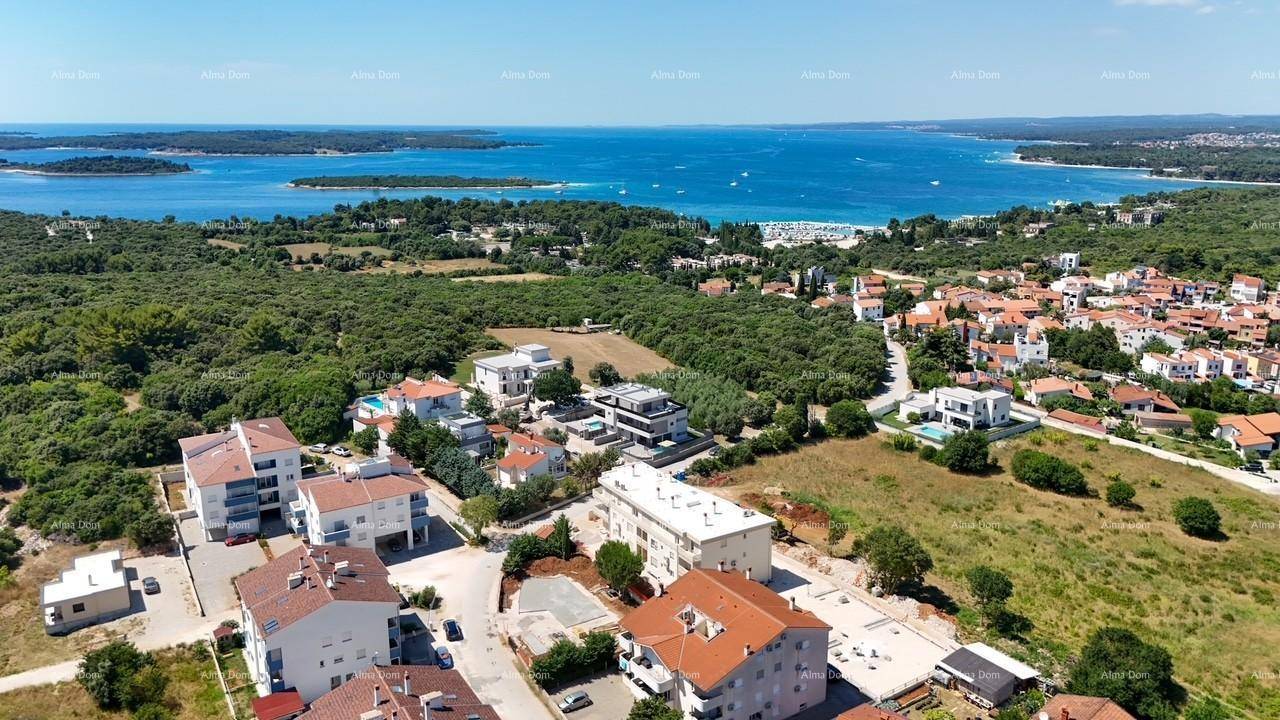 Luftaufnahme einer Küstensiedlung mit Wohngebäuden, viel Grün und dem Meer im Hintergrund unter blauem Himmel.