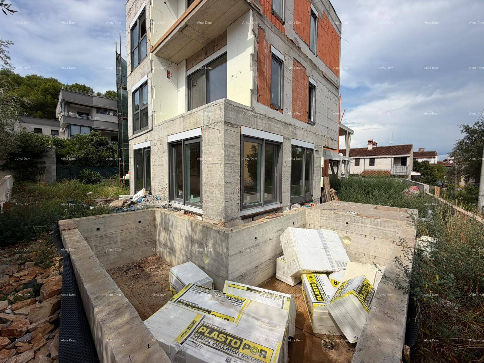 Im Bau befindliches Gebäude mit großen Fenstern und einer vorbereiteten Pool- oder Kellergrube im Vordergrund.