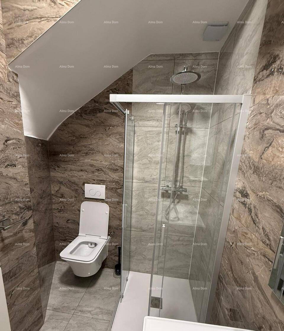 Badezimmer mit Duschkabine und wandhängender Toilette unter einer Dachschräge, braune Wandfliesen.