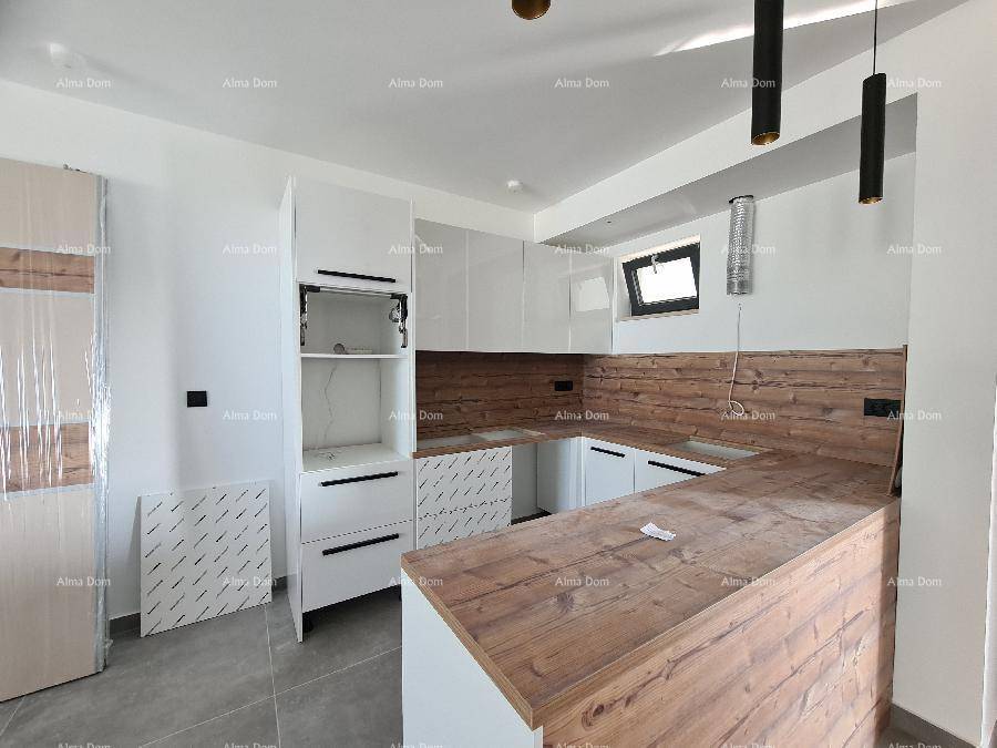 Moderne Küche im Aufbau mit weißen Schränken, Holzoptik-Arbeitsplatten und Fenster.