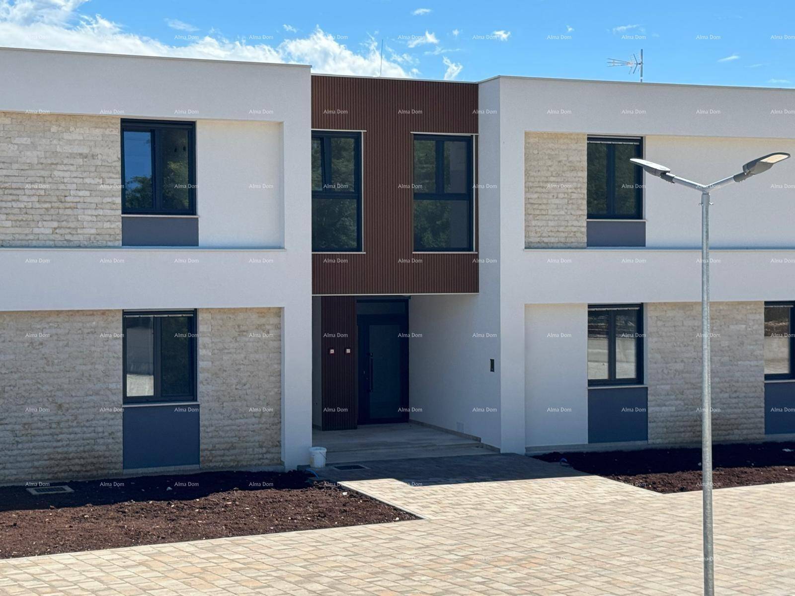 Eingangsbereich eines modernen Gebäudes mit heller Fassade und dunklen Fensterrahmen.