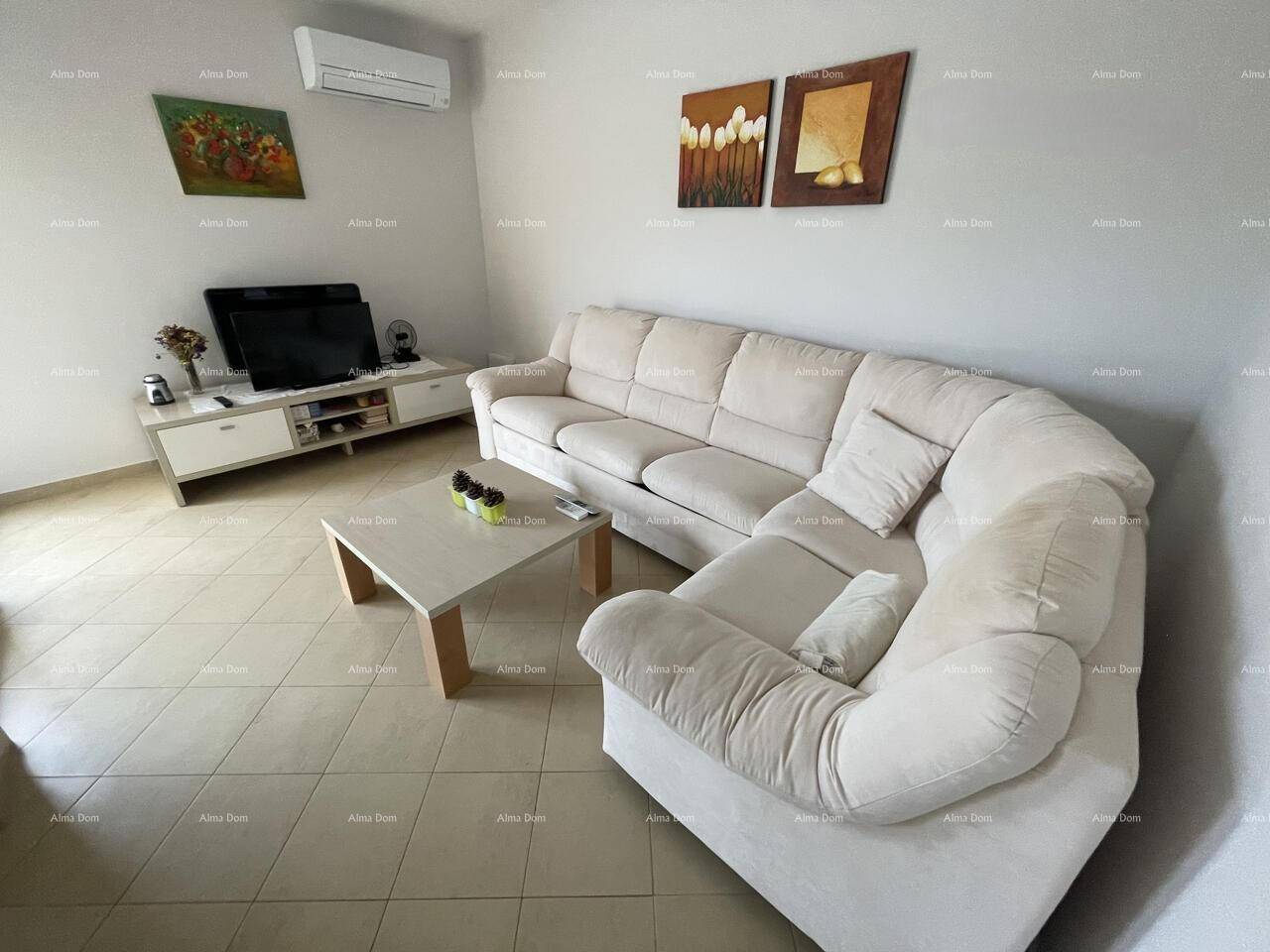 Komfortables Wohnzimmer mit großem Ecksofa, Fliesenboden und Klimaanlage für angenehmes Raumklima.