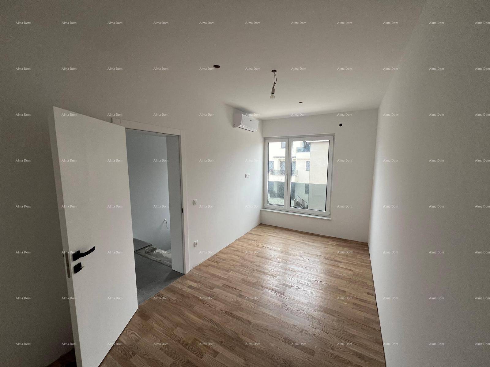 Leeres Zimmer mit Parkettboden, weißen Wänden, Fenster und einer Klimaanlage an der Wand.