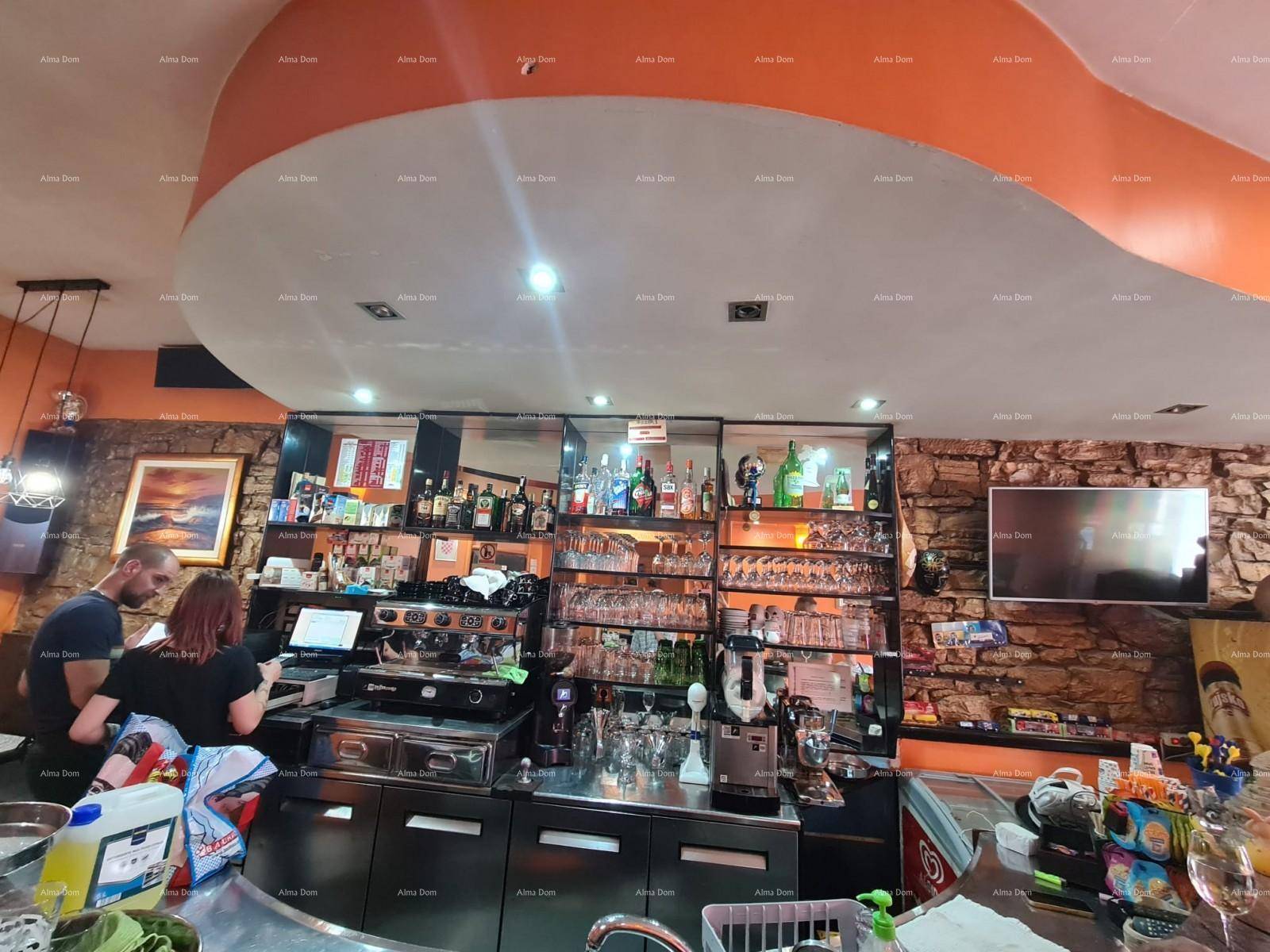 Innenansicht einer Bar mit gut gefüllten Regalen, einer Kaffeemaschine und einem Fernseher an der Wand.