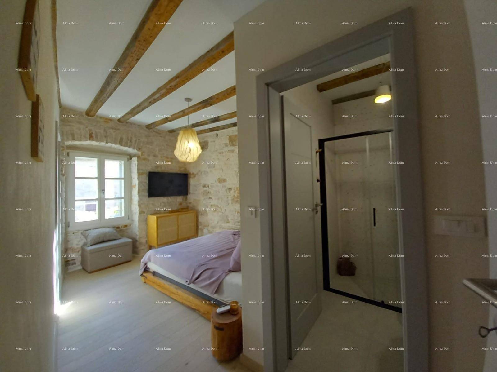 Schlafzimmer mit Holzbalkendecke, Steinwand und Zugang zu einem modernen Badezimmer.