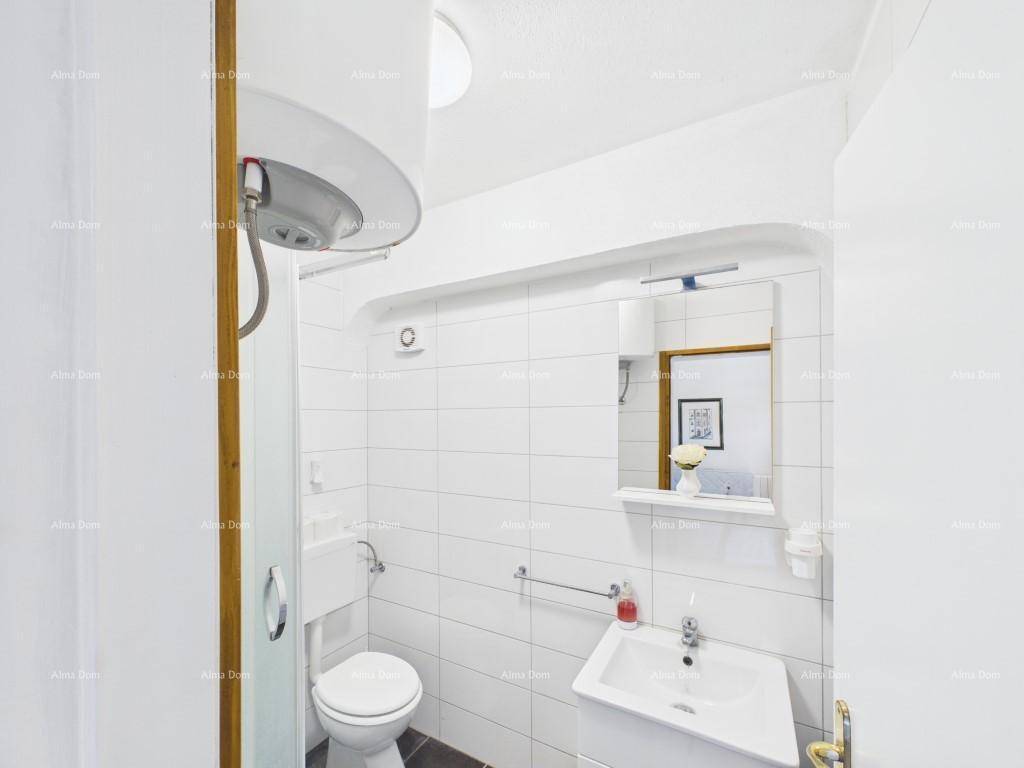 Kleines, hell gefliestes Badezimmer mit WC, Waschbecken und Duschbereich, ausgestattet mit Warmwasserboiler.