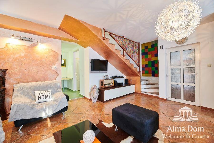 Wohnbereich mit Treppe, Sofa und dekorativen Elementen in warmen Farbtönen auf Fliesenboden.