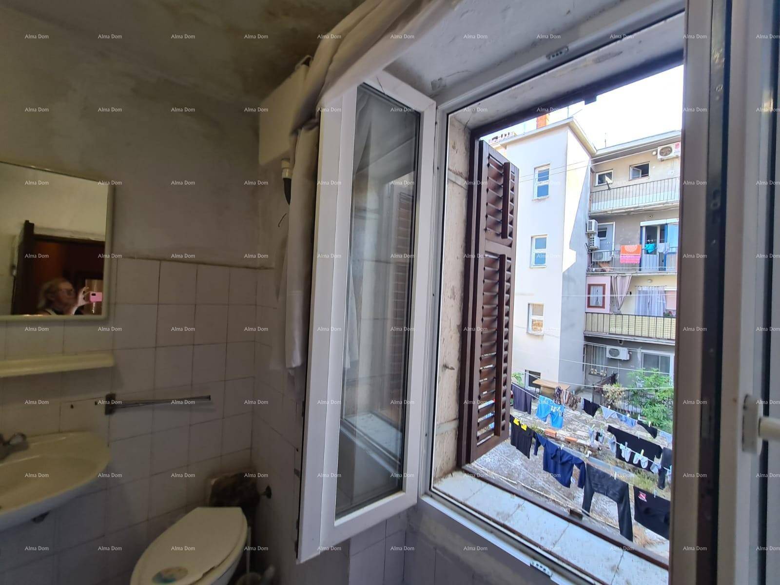 Badezimmer mit weißen Fliesen, Toilette, Waschbecken und einem Fenster mit Blick auf den Innenhof.