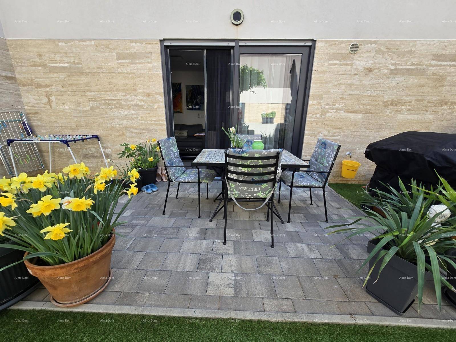 Möblierte Terrasse mit Esstisch und Stühlen, umgeben von Topfpflanzen und Kunstrasen.