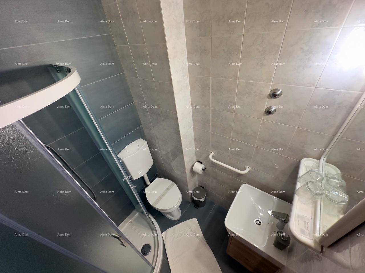 Badezimmer mit Duschkabine, WC und Waschbecken, ausgestattet mit grauen Fliesen und einem Haltegriff.