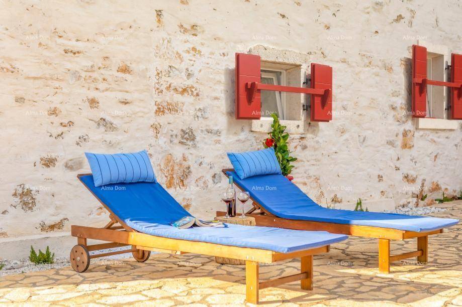 Zwei Sonnenliegen auf einer gepflasterten Terrasse vor der rustikalen Steinfassade des Hauses.