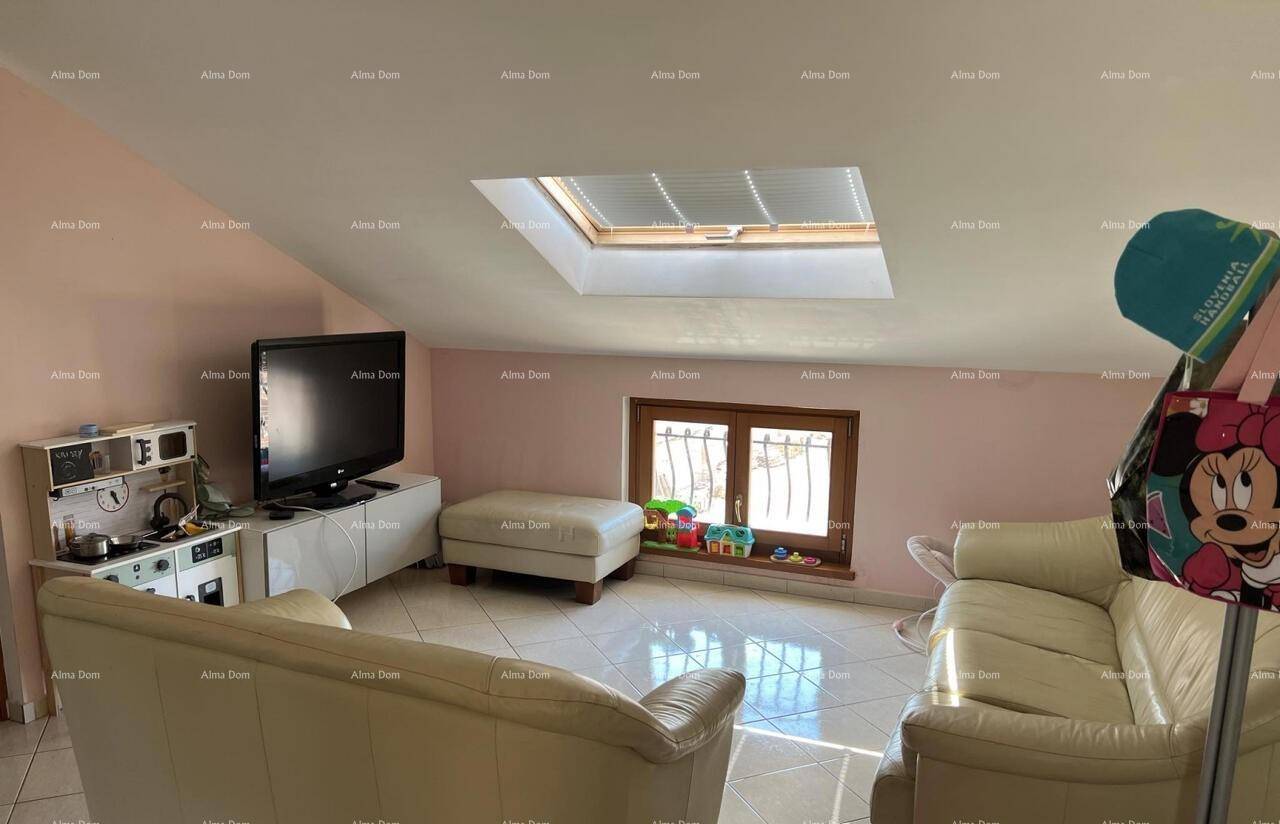 Gemütliches Wohnzimmer im Dachgeschoss mit Sofa, Fernseher und einem Dachfenster für viel Licht.
