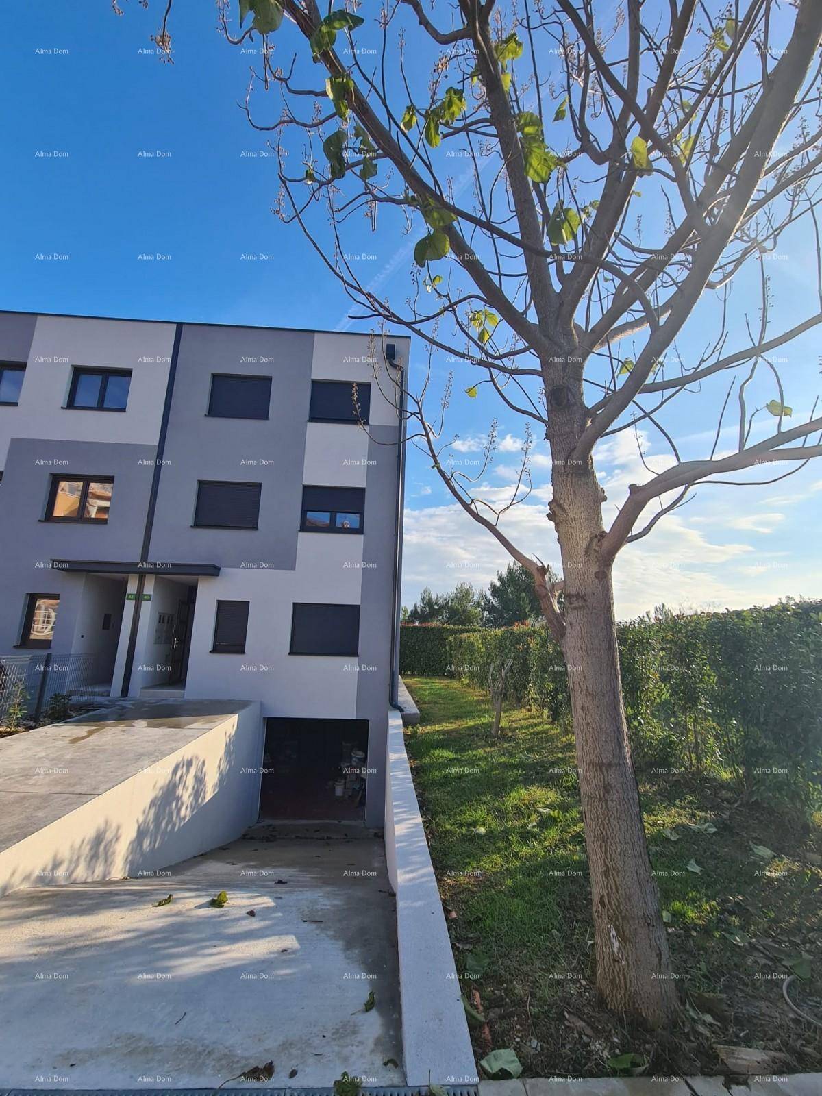 Vorderansicht eines modernen Gebäudes mit Zufahrt zur Tiefgarage und einem Baum im Vordergrund.