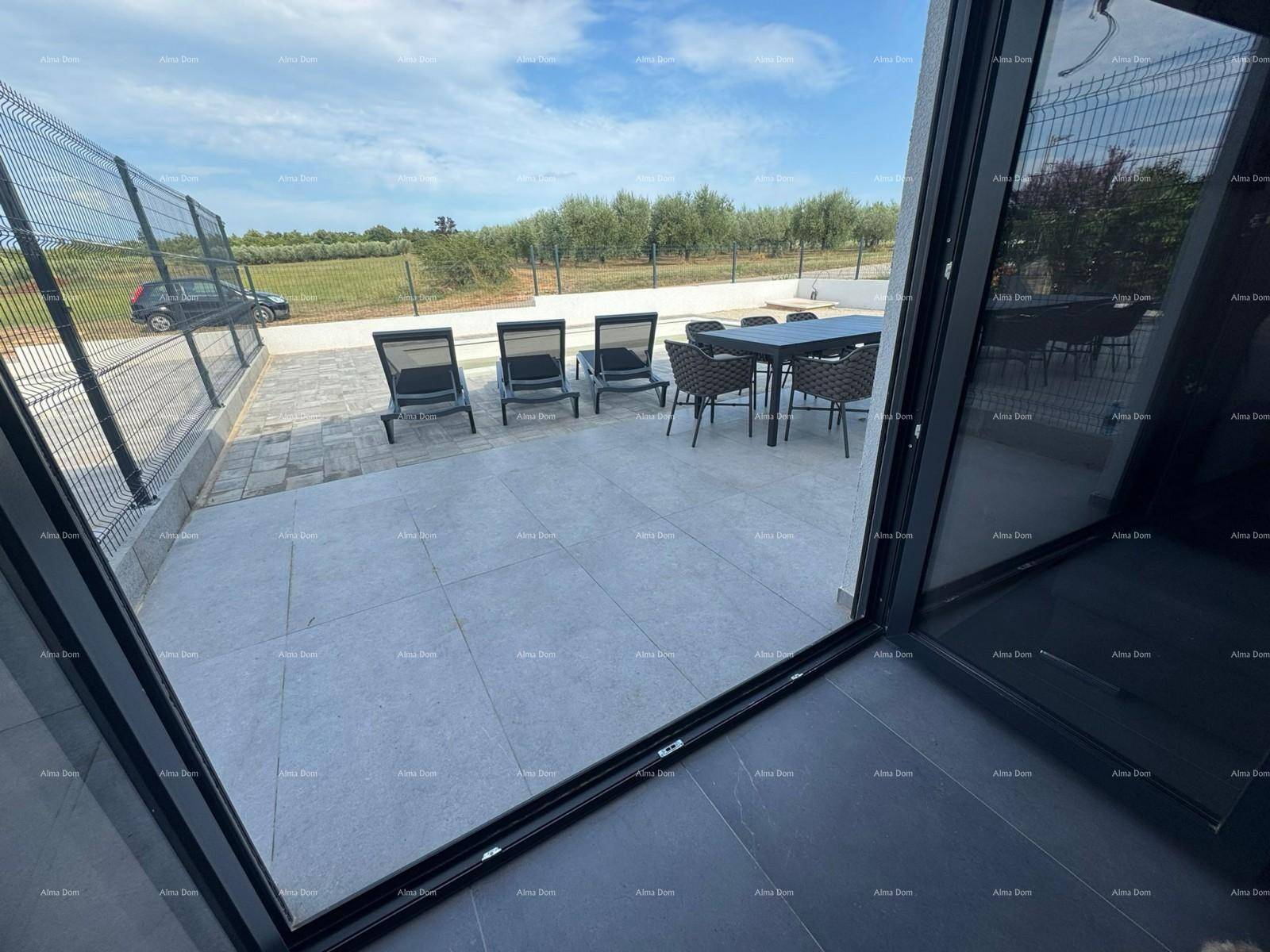 Blick aus dem Innenraum auf die sonnige Terrasse mit Esstisch und Liegestühlen.
