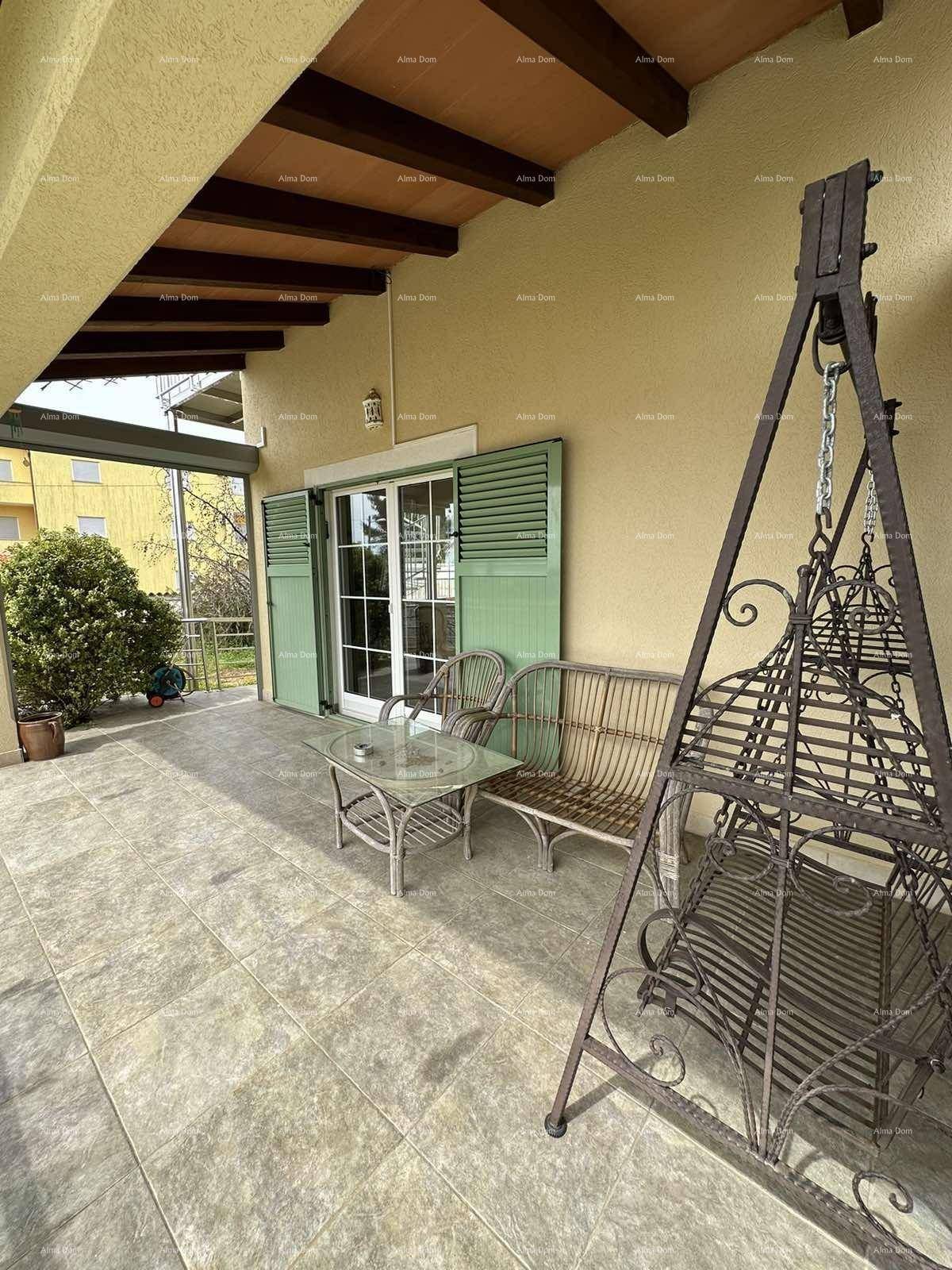 Überdachte Terrasse mit gefliestem Boden, Korbmöbeln und einem dekorativen Schaukelgestell.