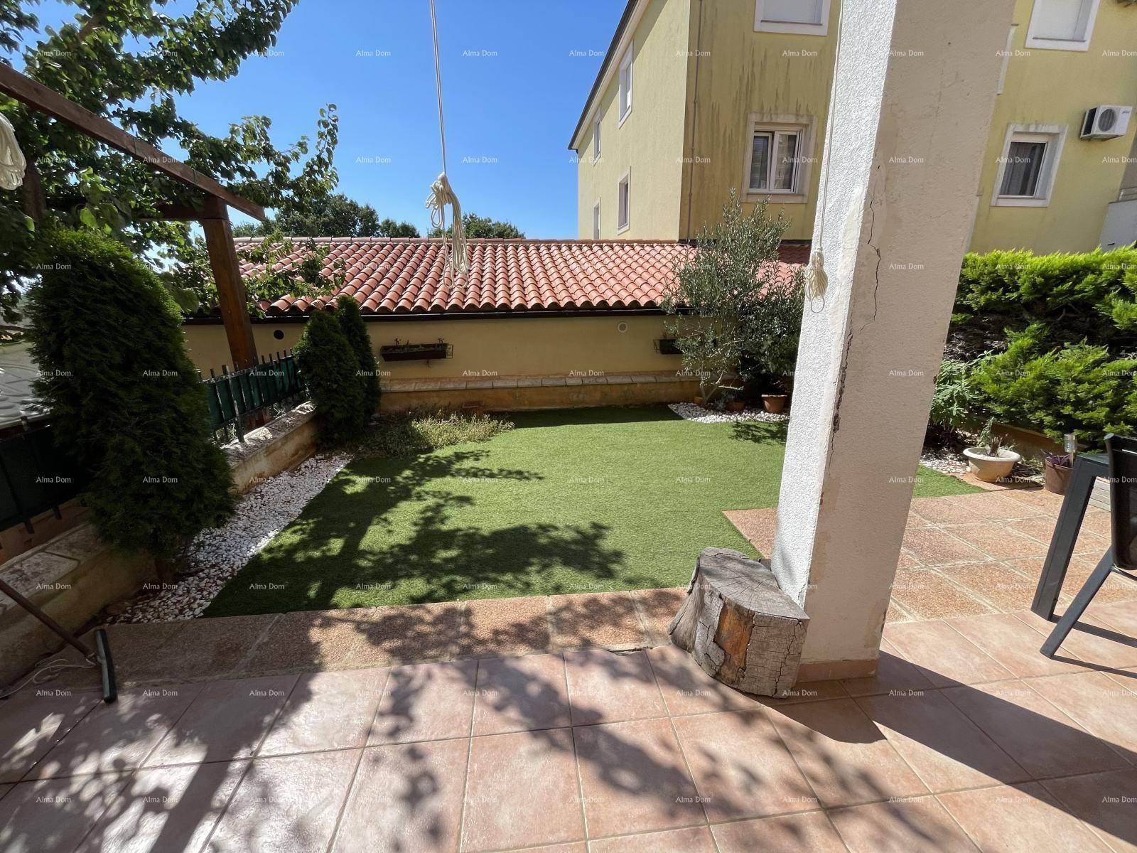 Sonniger Garten mit Kunstrasenfläche und gepflasterter Terrasse, umgeben von mediterraner Vegetation.