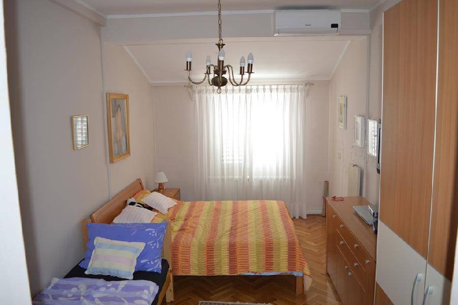Helles Schlafzimmer mit Holzboden, Doppelbett und einem zusätzlichen Einzelbett, ausgestattet mit Klimaanlage.