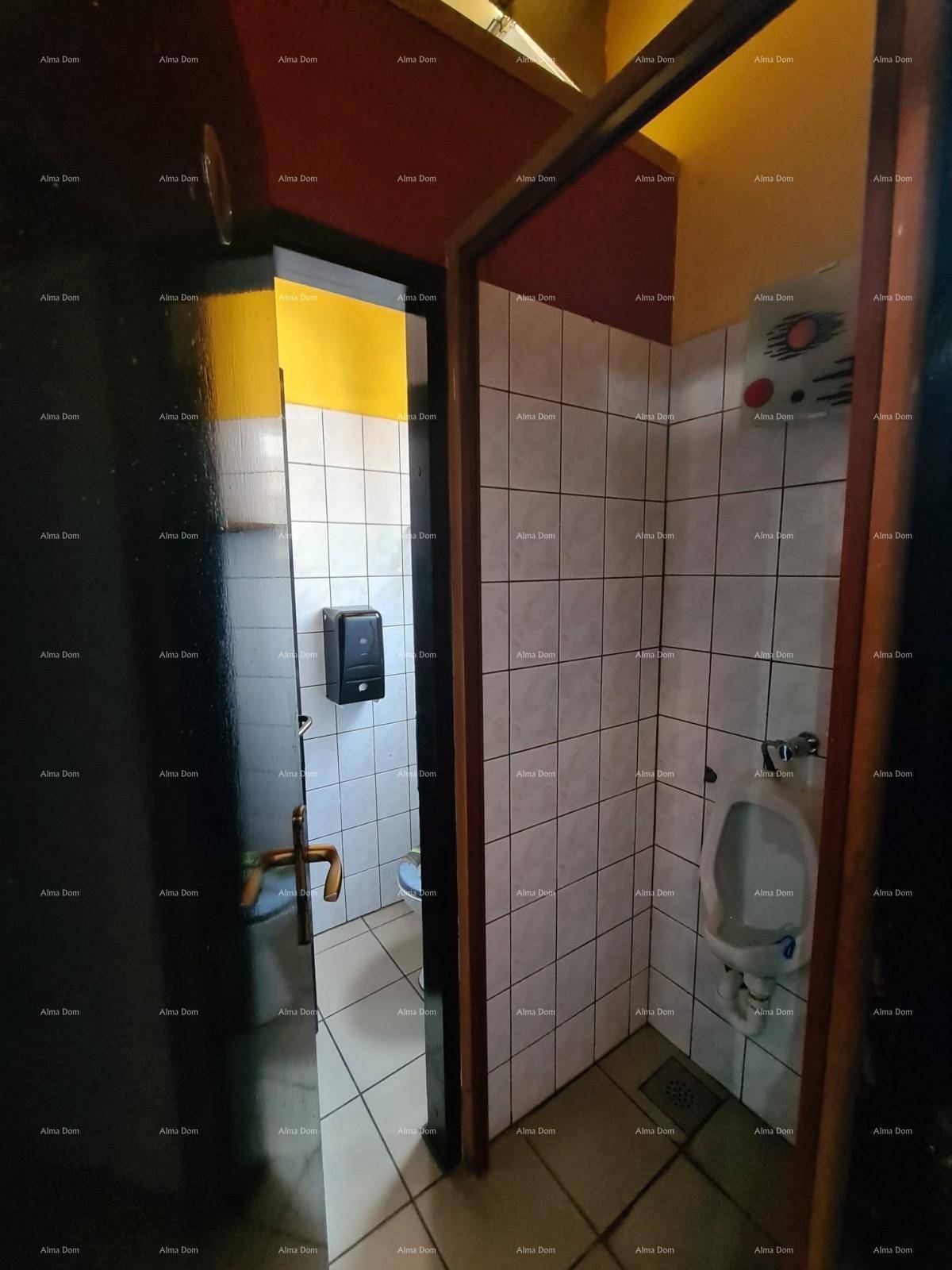 Herrentoilette mit weißen Fliesen, einem Urinal und einem Fenster für natürliche Belüftung.