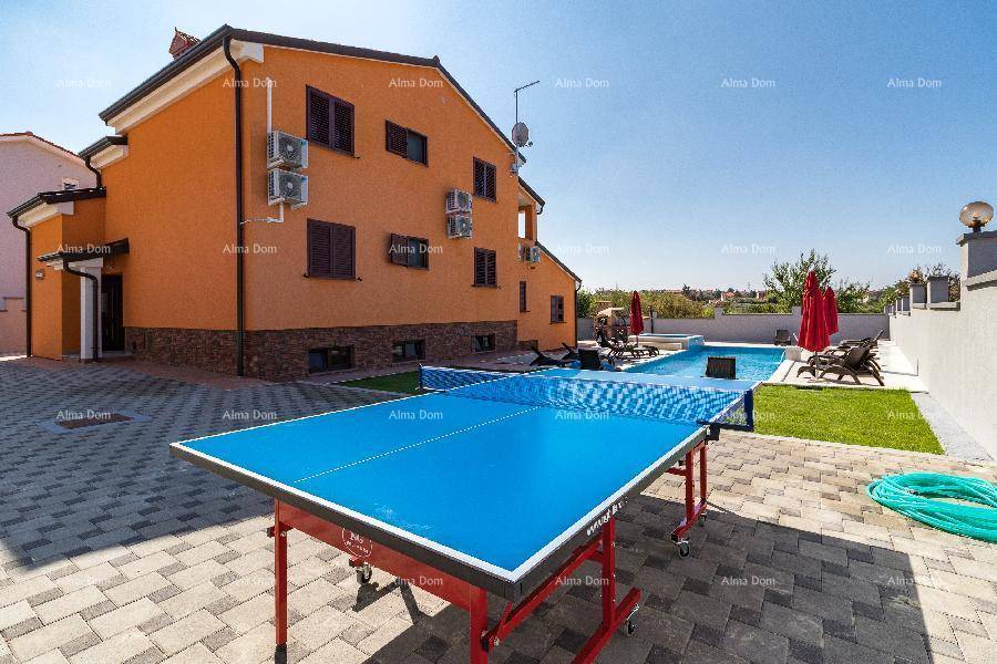 Außenbereich des Hauses mit Tischtennisplatte, Pool und Liegestühlen unter blauem Himmel.