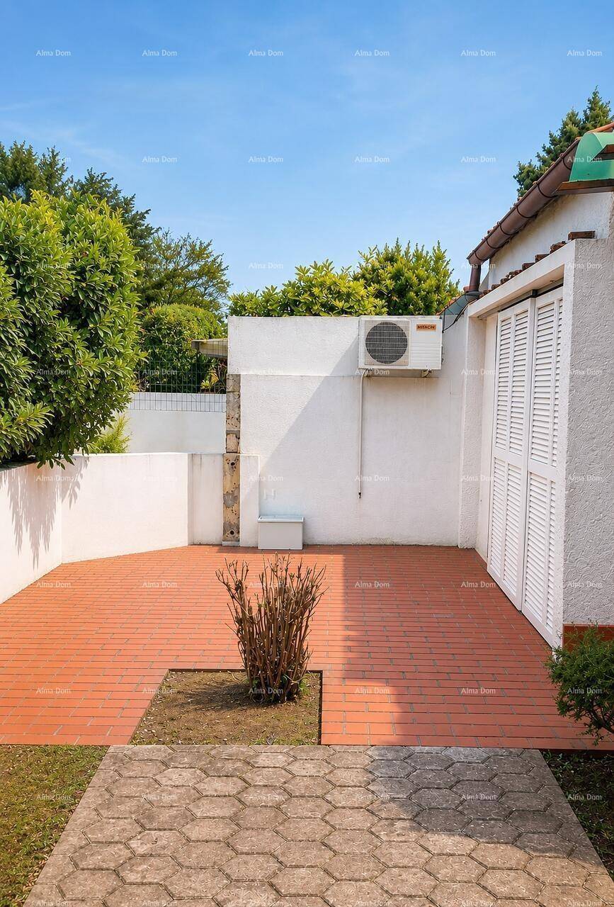 Sonniger Außenbereich mit Terrassenboden, kleiner Bepflanzung und Klimaanlage an der Wand.