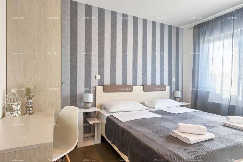 Helles Schlafzimmer mit Doppelbett, gestreifter Tapete und Arbeitsbereich am Fenster.