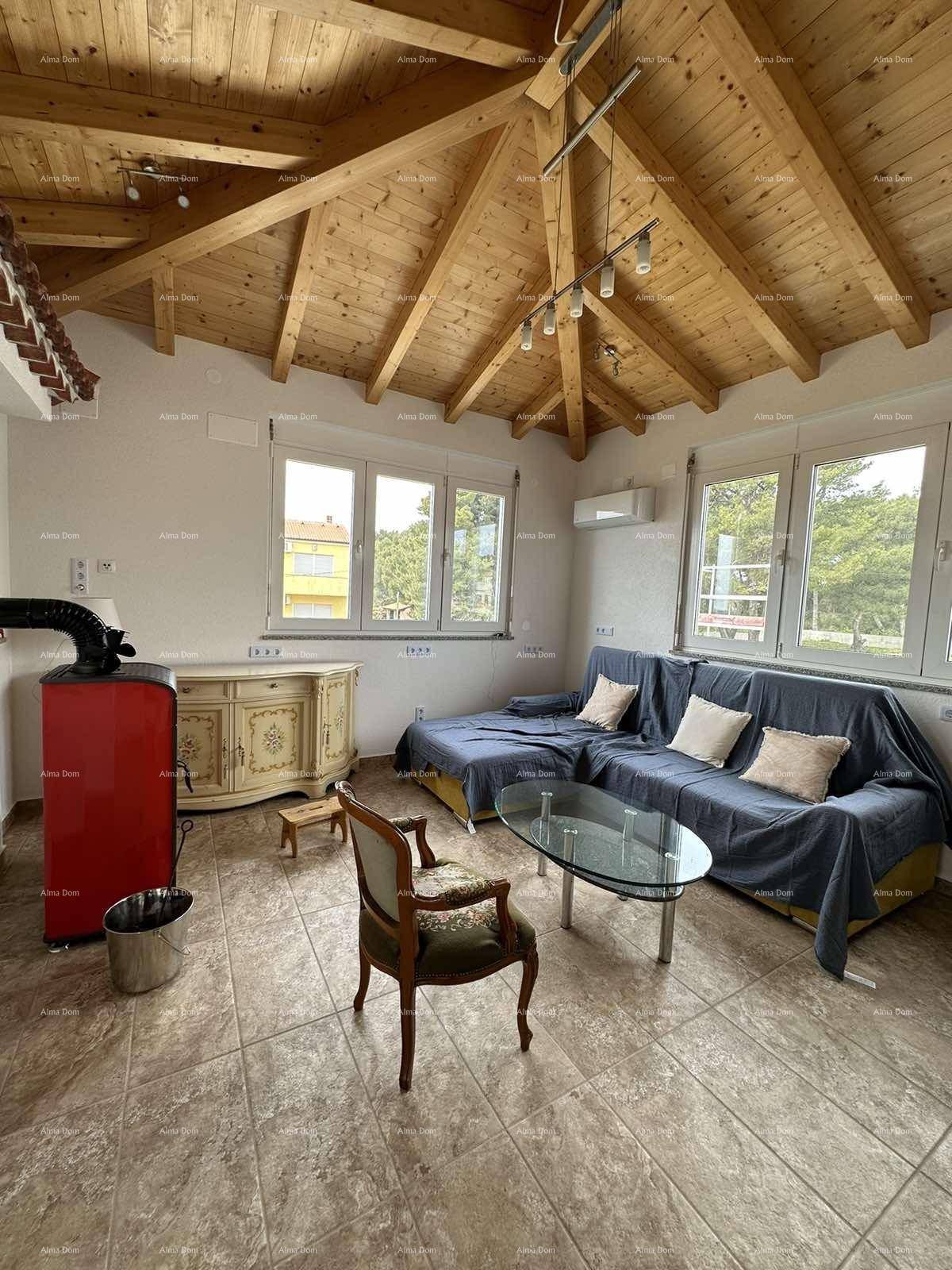 Gemütliches Wohnzimmer mit Holzbalkendecke, Fliesenboden und einem roten Kaminofen.