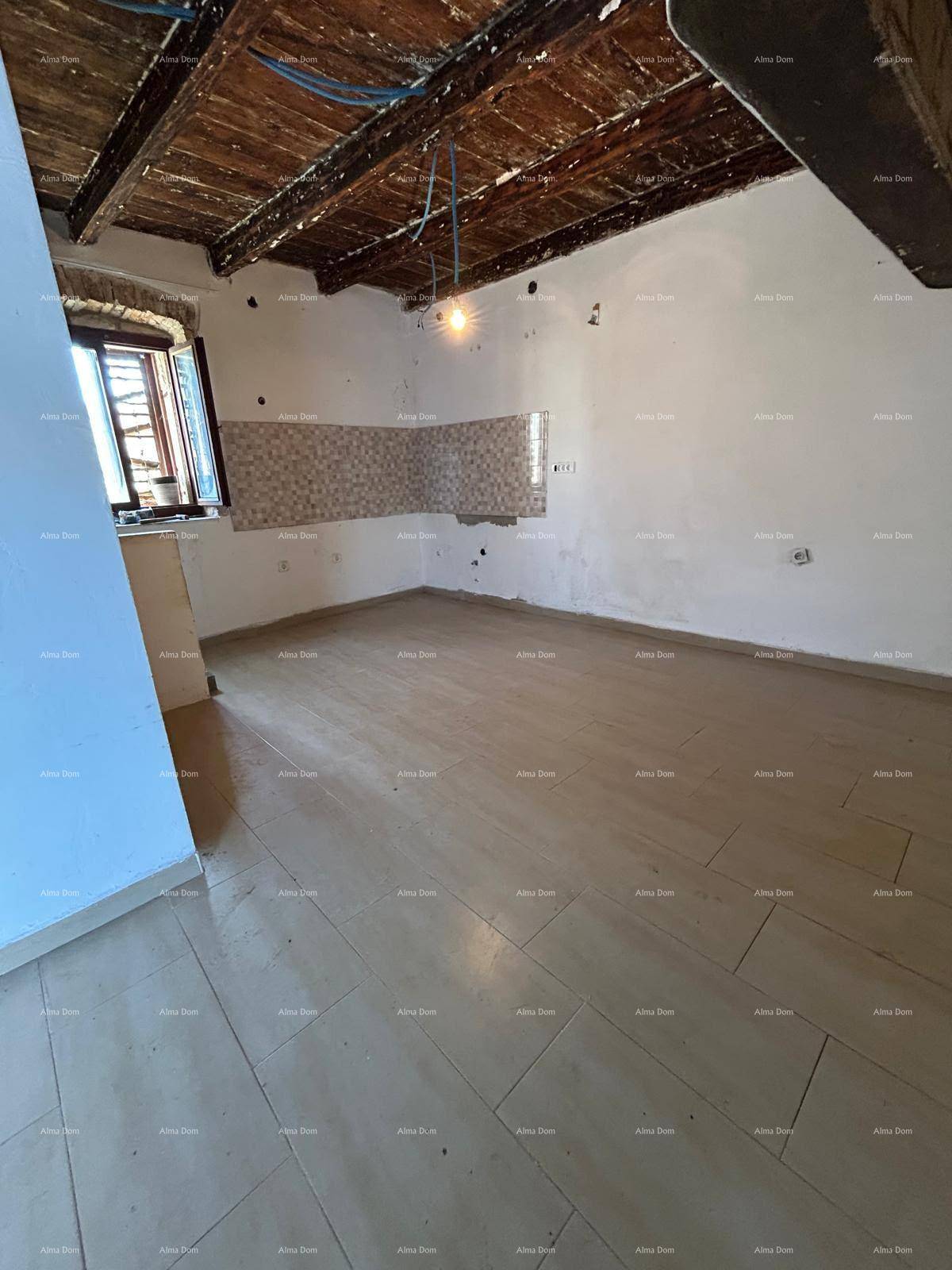 Großer Küchenraum im Rohbau mit Fliesenboden, sichtbaren Holzbalken und Fenster.