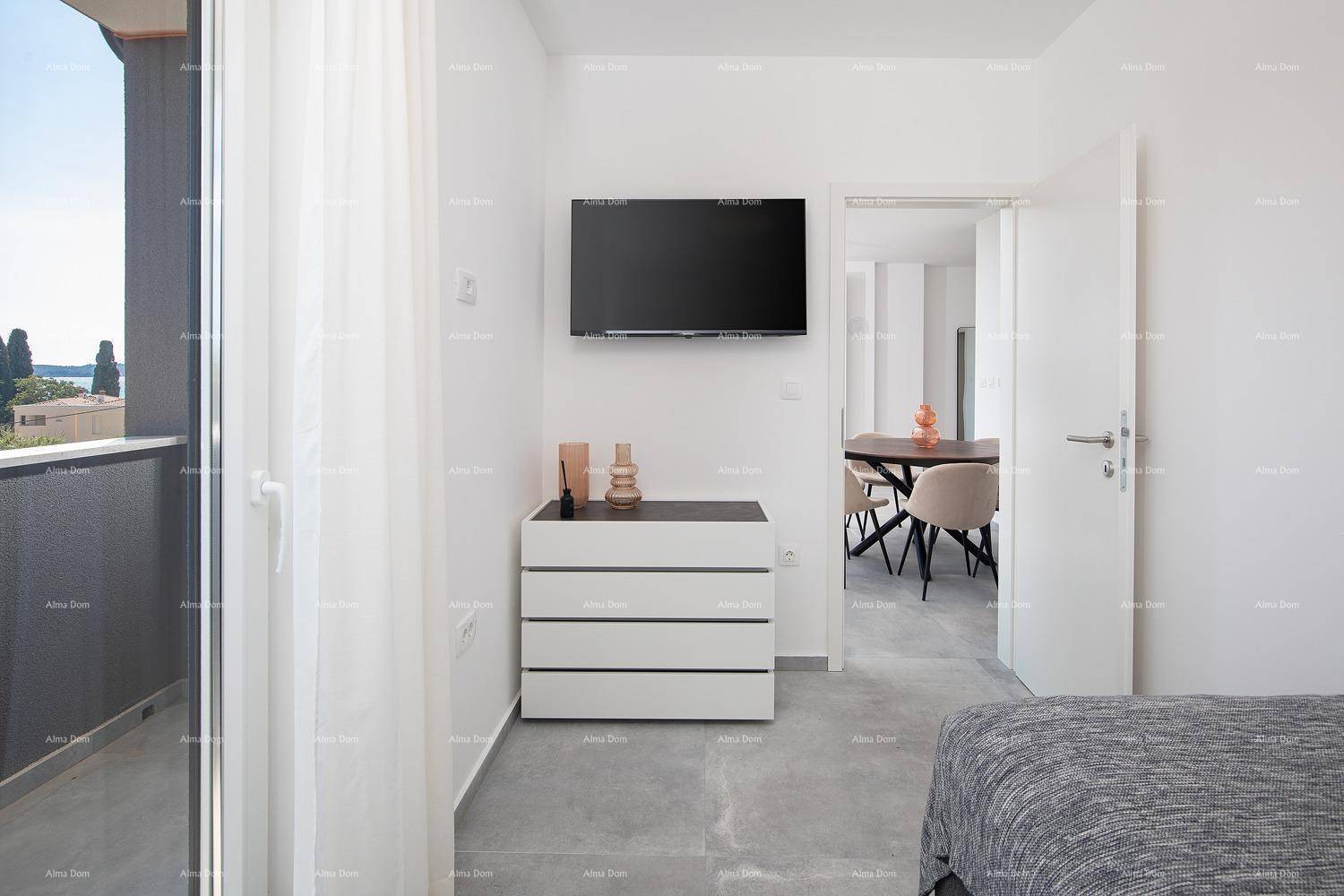 Schlafzimmer mit Kommode, Fernseher und Zugang zum Wohnbereich sowie einem Balkon.