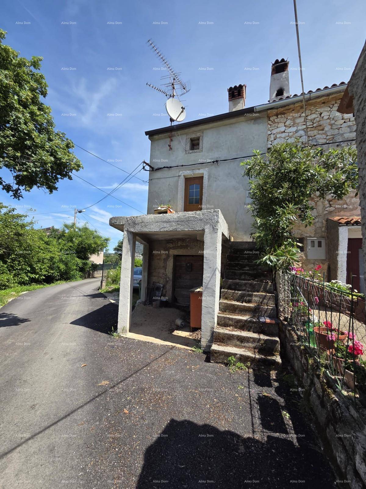 Altes Steinhaus mit Außentreppe und überdachtem Bereich, direkt an einer schmalen Straße gelegen.