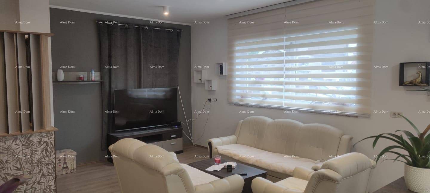Gemütliches Wohnzimmer mit beigem Sofa, Fernseher und großem Fenster mit Jalousien.