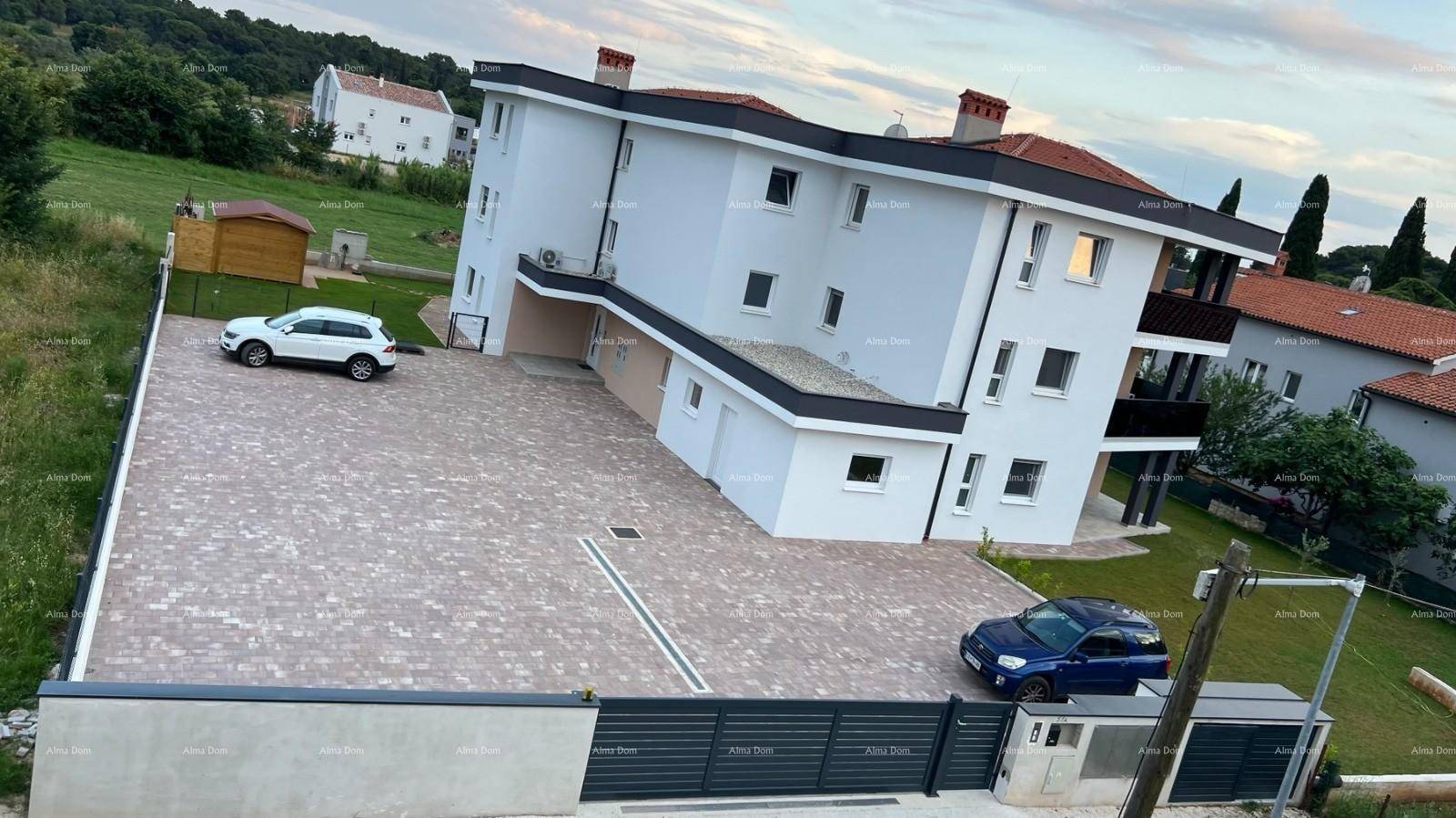Vogelperspektive eines modernen Wohngebäudes mit großem Parkplatz und umliegender Grünfläche.
