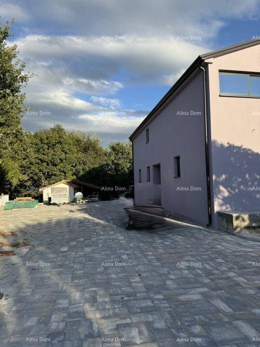 Seitenansicht des Hauses mit gepflastertem Bereich und angrenzendem Grün unter bewölktem Himmel.