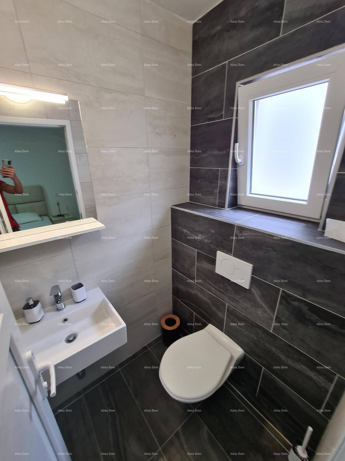 Modernes Badezimmer mit Fenster, dunklen Fliesen, Waschbecken und wandhängendem WC.