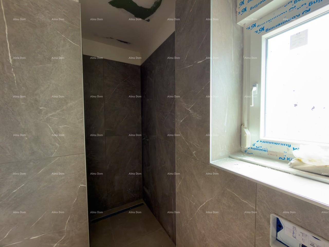 Unfertiges Badezimmer mit grauen Fliesenwänden und vorbereitetem Bereich für eine Dusche.