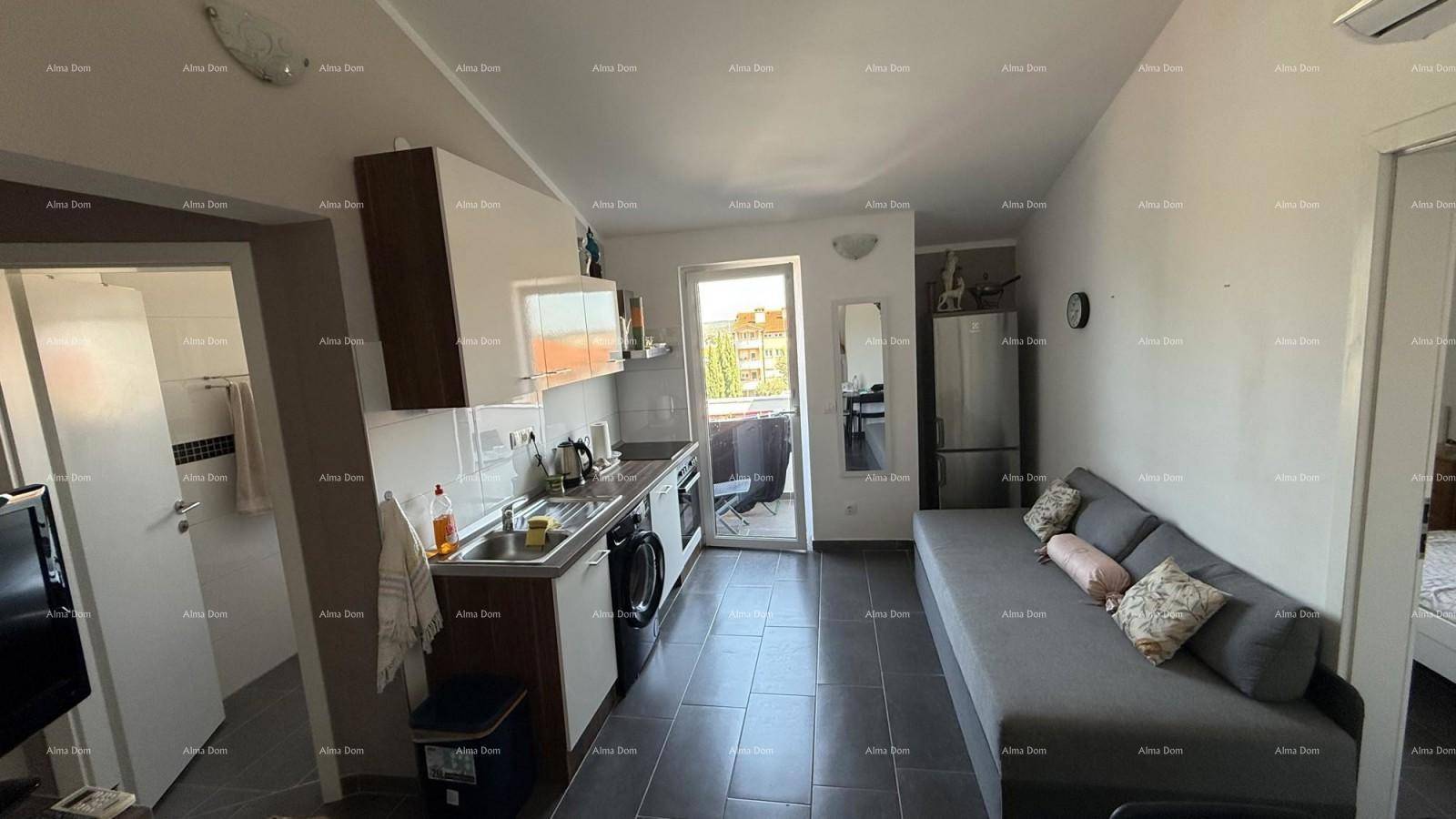 Offener Wohn- und Küchenbereich mit Sofa, kleiner Küchenzeile und Zugang zu einem Balkon.