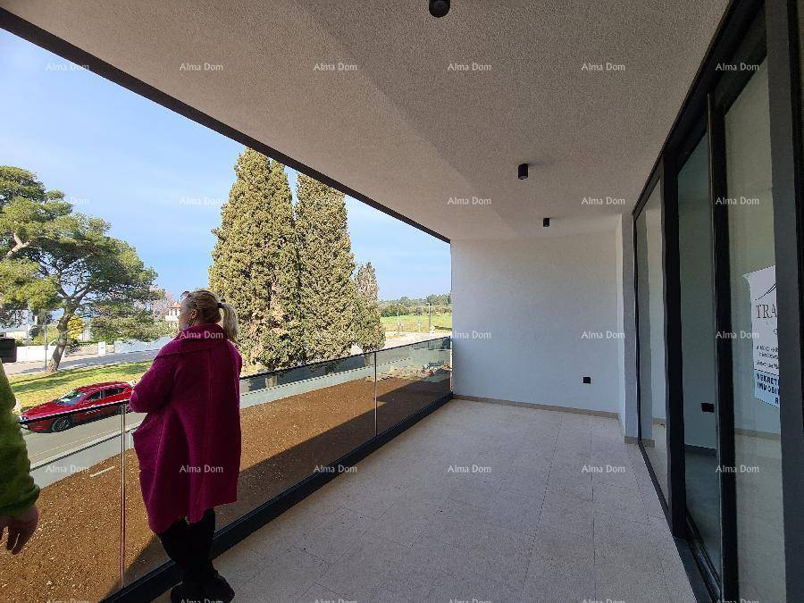 Geräumiger Balkon mit Glasgeländer und Blick auf die Küste und grüne Bäume.