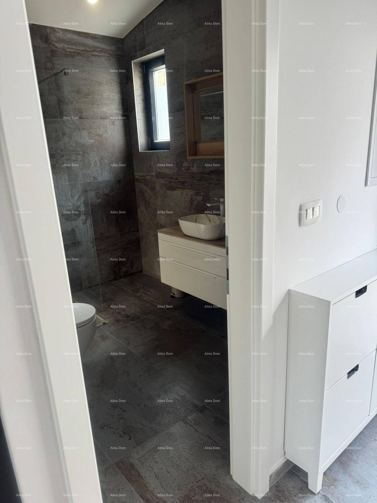 Blick vom Schlafzimmer in ein modernes Badezimmer mit dunklen Fliesen und Fenster.