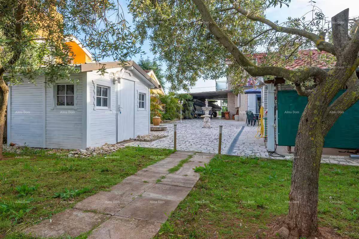 Gepflegter Gartenbereich mit weißem Gartenhaus, Bäumen und gepflastertem Weg.