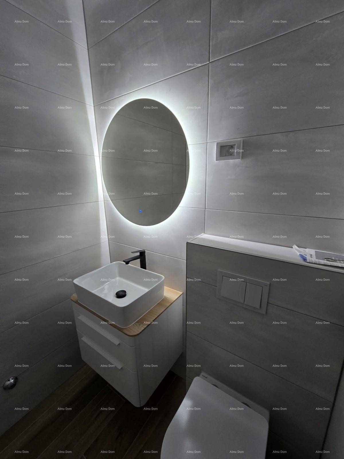Elegantes Badezimmer mit runden, beleuchteten Spiegel, modernem Waschtisch und grauen Wandfliesen.
