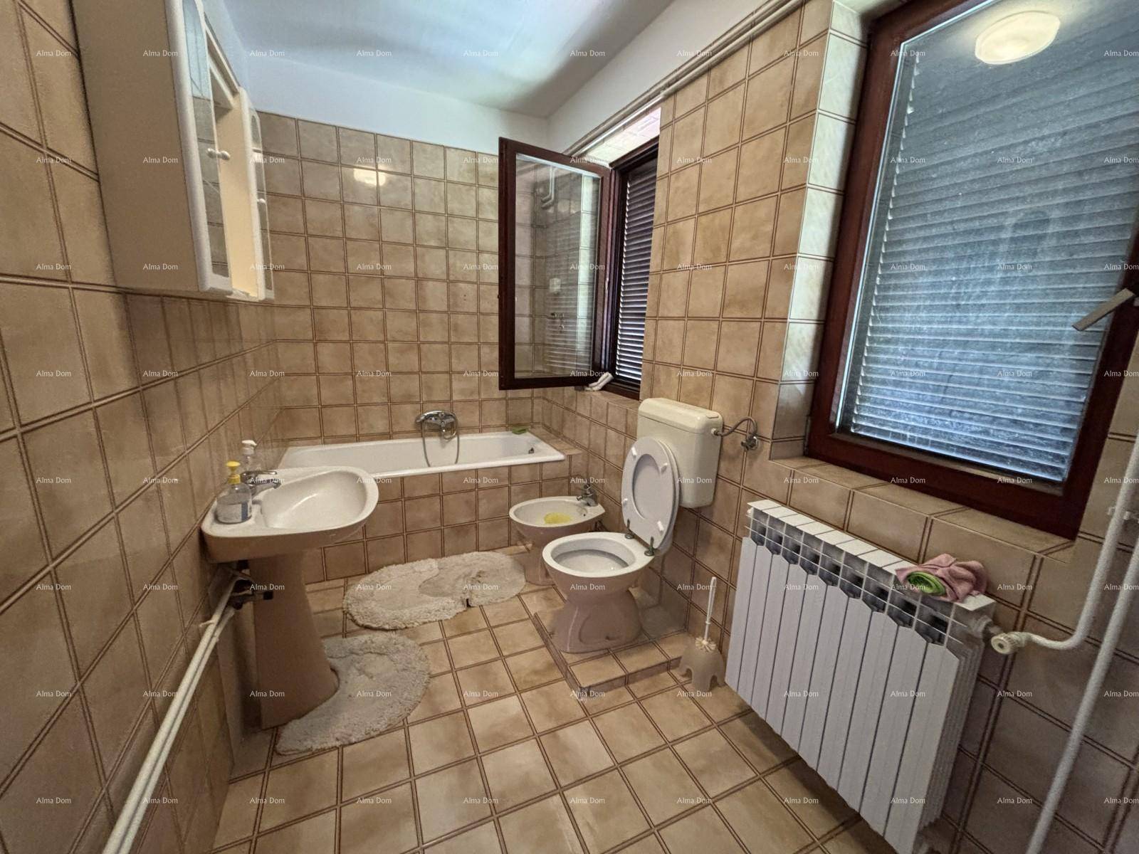 Badezimmer im Stil der 80er Jahre mit beigefarbenen Fliesen, Badewanne, Bidet und Fenster.