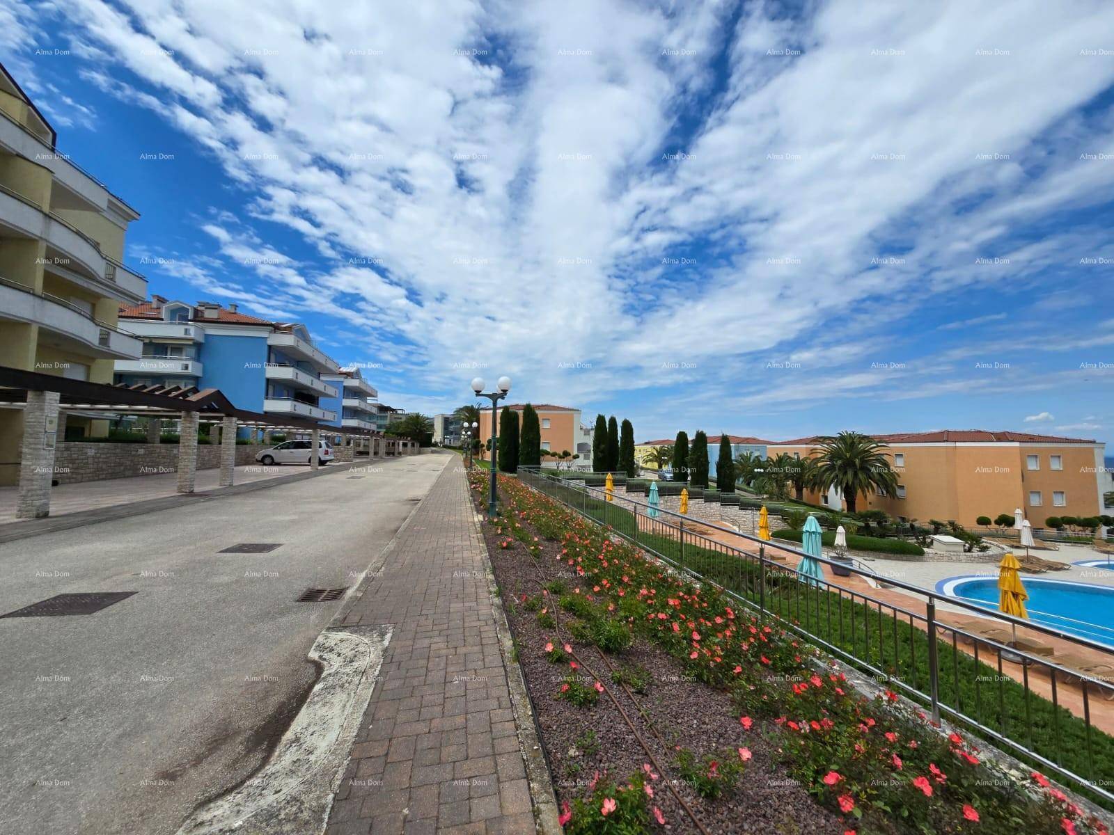 Gepflasterter Weg innerhalb der Anlage mit Blick auf die Gebäude, Grünflächen und das Meer.