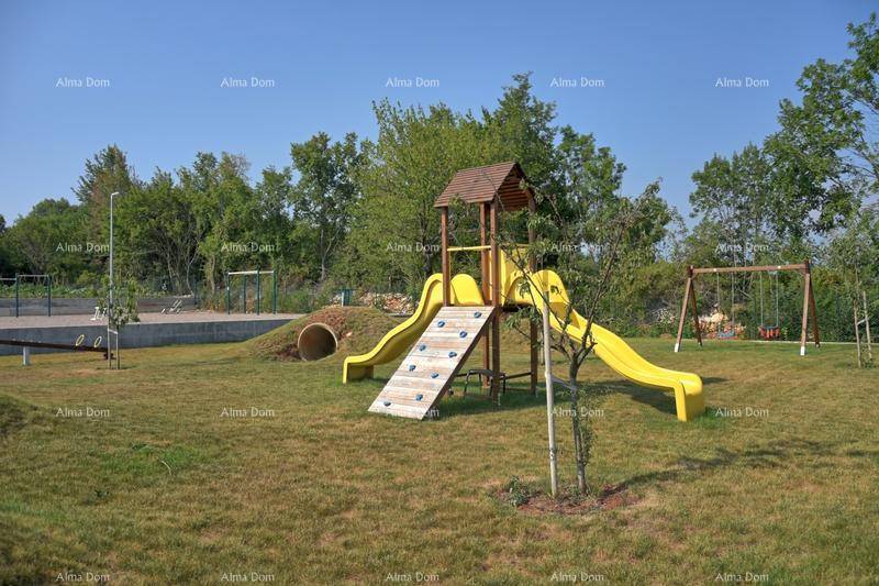 Kinderspielplatz mit Rutschen und Schaukeln, umgeben von einer grünen Wiese.