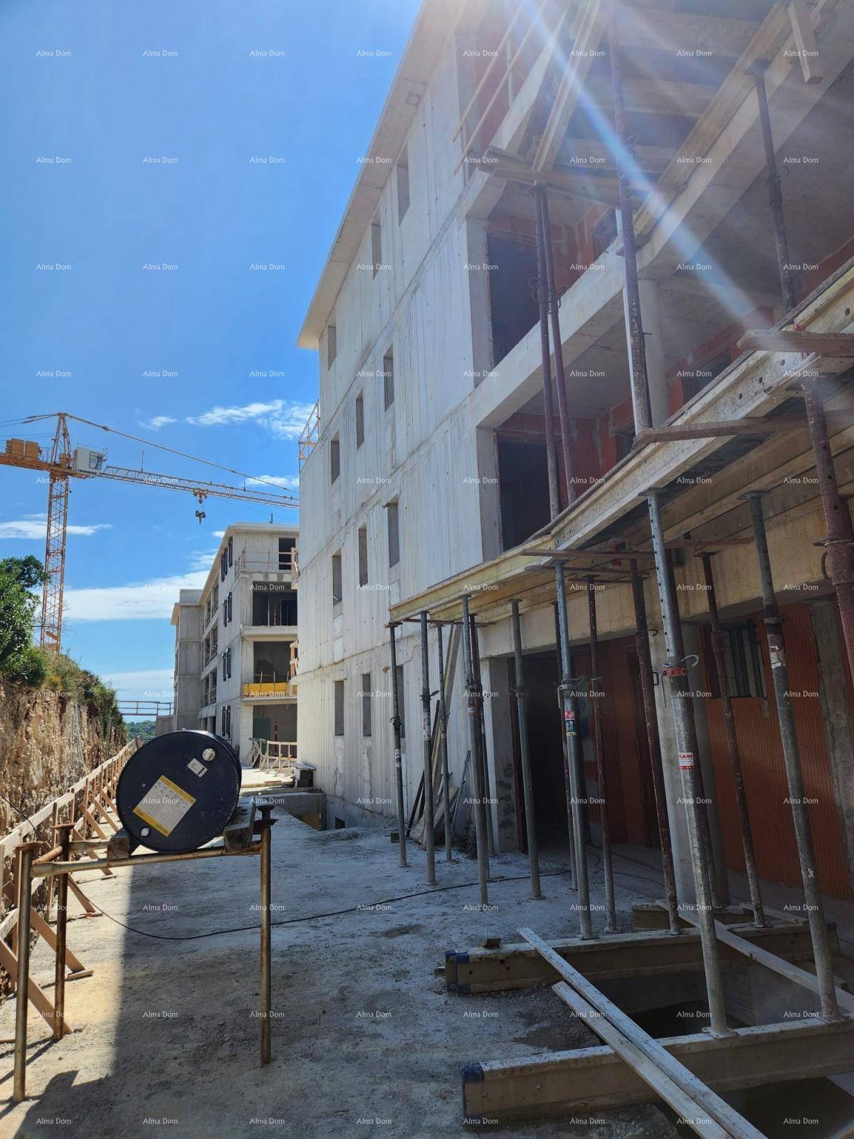 Mehrere Gebäude im Rohbau mit Gerüsten und Baumaterialien unter strahlend blauem Himmel.