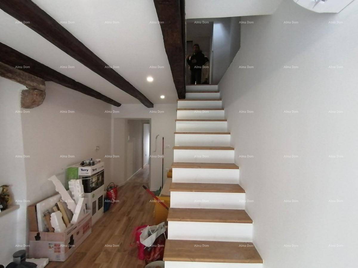 Wohnbereich mit offener Treppe, sichtbaren Deckenbalken und hellem Holzboden.