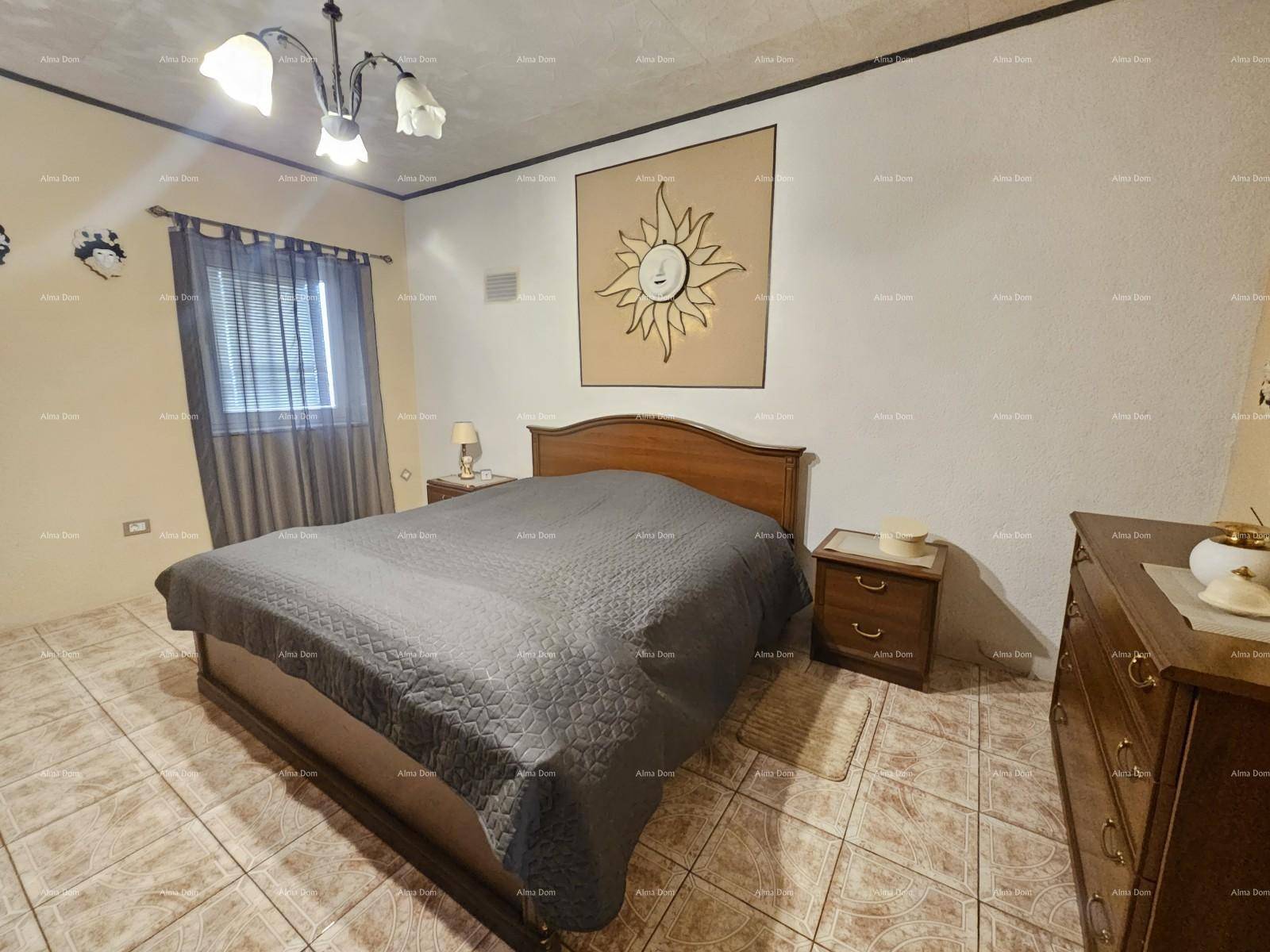 Schlafzimmer mit Doppelbett, Nachttischen, Kommode und Fliesenboden, dekoriert mit einem Sonnenmotiv.